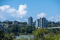 A panoramic view of a vibrant urban landscape featuring contemporary high-rise buildings nestled amongst dense green foliage under a bright sky, Garry Point park, Richmond, BC, Canada [IBR125424502]