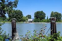 A calm river flows past weathered wooden pilings leading to a small ferry dock with a building and trees on the opposite bank, Dyke Rd, Surrey, BC V4N 4R 1, Canada [IBR125424504]