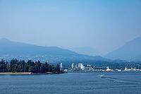 A small seaplane departs from the calm waters of Vancouver's harbor, with forested Stanley Park and distant mountains forming a scenic backdrop, Canada place, North Vancouver, BC Canada [IBR125424523]