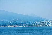 A wide view of the Vancouver skyline with lush green mountains in the background and ships sailing on the ocean, Canada place, North Vancouver, BC Canada [IBR125424533]