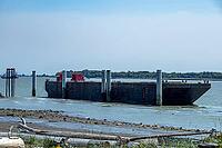 A wide, flat-bottomed barge with red structures on deck is moored in a tranquil bay with a distant forest and clear sky overhead, Garry Point park, Richmond, BC, Canada [IBR125424537]