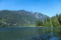 A vast, calm lake reflects the surrounding dense evergreen forests and majestic mountains under a bright, cloudless sky, kettle Valley trail, BC Canada [IBR125424539]