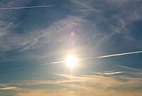 Sun illuminates cirrus clouds and airplane contrails against a blue sky, creating a lens flare [IBR125424553]