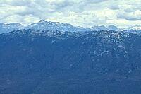 Expansive view of rugged mountain peaks with patches of snow, receding into a hazy horizon above a deep blue coniferous forest, Glacier Whistler, BC, Canada [IBR125424558]