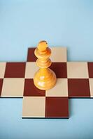 A yellow wooden king on a brown and beige chessboard against a light blue background [IBR125424559]