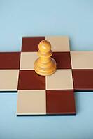 A yellow wooden pawn on a brown and beige chessboard with a light blue background [IBR125424564]