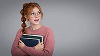 A redheaded student with freckles and round glasses holds two books against a pink sweater, looking upward with an animated expression against a gray studio setting. Cute smile, AI generated [IBR125424579]