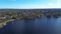 Aerial view showing village houses on the shore of a dark blue lake under a bright sky [IBR125436242]