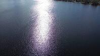 Sun reflecting on a lake surface creating a path of shimmering light, with land visible in the distance [IBR125436276]
