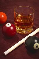 A glass of whiskey sits next to three billiard balls numbered 5, 7, and 8 on a dark table. A white cue stick lies across the table. This scene captures a moment of leisure [IBR125437990]