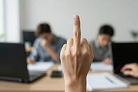 Workplace rebellion with rude middle finger gesture in corporate office shows toxic employment culture, job burnout and extreme employee frustration, foreground hand displaying offensive sign towards camera, unfocused colleagues sitting at desks in backgr [IBR125446416]