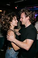 Authentic young couple dancing with joyful intimacy on a vibrant nightclub floor, dynamic motion of wavy brunette hair and shared affectionate smiles, the close embrace and tender eye contact manifest profound romantic chemistry amidst energetic club cult [IBR125446417]
