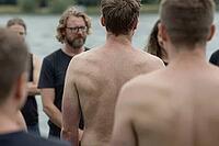 Vulnerable men gathering in a supportive circle by a lake for emotional healing, psychological growth, somatic body awareness, mindful brotherhood, an exposed bare back stands centered amidst attentive listeners as a metaphor for deep emotional transparen [IBR125446418]
