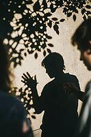 Shadow play and expressive hand gestures on textured stucco reflect nonverbal communication, emotional nuance, interpersonal resonance and internal dialogue, high contrast sunlight projects botanical foliage patterns above an introspective silhouette evok [IBR125446423]