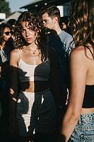 Youthful detachment and introspective solitude amid a crowded festival crowd, direct gaze conveying emotional vulnerability, shadow patterns slice across the body as an existential barrier, an evocative metaphor for inner alienation within bustling social [IBR125446425]