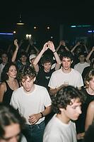 Young adults dancing in crowded nocturnal nightclub enjoying electronic music culture, collective euphoria and nocturnal social connection in club life, raised hands and synchronized movements express deep emotional release within dark ambient clubbing at [IBR125446426]