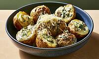 Freshly baked potatoes with melted cheese and green herbs in a ceramic bowl, AI generated [IBR125446429]