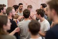 Dynamic group debate and social interaction among diverse young men indoors, expressive faces convey intense concentration, skepticism and dialogue, diverse individuals assemble in close proximity against a polished pink stone wall, shallow depth of field [IBR125446449]