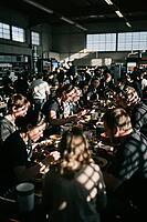 Communal dining in converted warehouse cafeteria, workers and creatives sharing meal along rustic tables under warm sunlight casting lattice shadows, collective lunch break uniting people across long wooden furniture, dynamic interplay of bright window gl [IBR125446462]