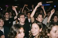 Youthful crowd celebration and collective euphoria during a live concert event, young people enjoying nightlife party atmosphere, raised arms moving rhythmically to musical beats within a dark club hall, smiling faces expressing pure ecstasy and authentic [IBR125446463]