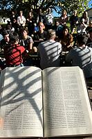 Scriptural outdoor study session uniting a diverse assembly under leafy foliage, open liturgical pages illuminated by cast beam shadows symbolize ancestral heritage intertwined with contemporary community contemplation, attentive listeners arranged in con [IBR125446469]