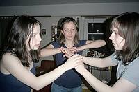 Youthful connection and synchronized nonverbal interaction between three young women, concentrated hand gesture dynamic during an indoor parlor game, triangular physical posture with direct flash illumination casting distinct shadows against the domestic  [IBR125446470]