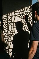 Shadow silhouette of a man cast upon a sunlit wall interlaced with intricate geometric lattice patterns, exploring themes of human consciousness, psychological fragmentation and the interplay between light and darkness, harsh chiaroscuro structures transf [IBR125446473]
