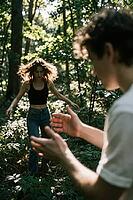Interpersonal connection and intuitive body language thrive in a secluded forest grove, where dappled sunlight illuminates organic youth interaction, motion blur of wild hair frames a woman spinning in freedom, open hands of an out-of-focus young man reac [IBR125446475]