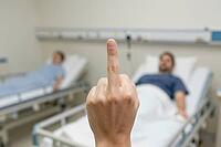 Middle finger gesture in a clinical hospital room confronting systemic healthcare failure, overworked nursing staff and neglected recovery patients, medical staff burnout during severe understaffing crisis, profound indignation toward administrative auste [IBR125446477]