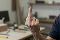 Workplace rebellion and intense frustration in a craft workshop, an anonymous person shows an explicit middle finger gesture toward authority, professional dissatisfaction and vocational stress collide with corporate pressure, hand anatomy reveals tension [IBR125446478]