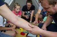 Pediatric care and health examination during child play, a caring hand gently inspects an extended arm for minor injuries or allergic skin reactions, the supportive touch embodies parental vigilance alongside tactile empathy, children and guardians gather [IBR125446479]