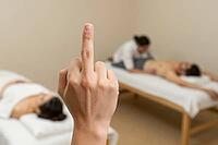 Rebellious middle finger gesture before relaxing spa treatment, rejecting wellness culture, disruptive nonverbal provocation, stress relief defiance, stark conceptual contradiction between visceral aggression and meditative tranquility, an anonymous hand  [IBR125446485]