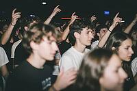 Collective euphoria and youth culture in vibrant nightlife club concerts, enthusiastic teenagers raise arms in unison during live music performance, energetic atmosphere of adolescent escapism and emotional release in dimly lit venue spaces, blurred motio [IBR125446486]