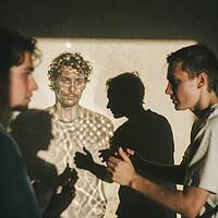 Interpersonal psychological resonance and perceptual duality unfold through illuminated human silhouettes, dynamic projection light revealing melancholic contemplation, young men interacting in deep ambient shadows, projected facial textures creating surr [IBR125446489]