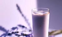 Tall glass holds creamy lavender milkshake. Soft purple lighting enhances calm mood. Blurred lavender sprig adds natural touch, AI generated [IBR125446491]