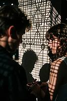 Interpersonal intimacy amidst geometric grid shadows, two lovers standing close in dramatic chiaroscuro illumination, contemplative longing and delicate emotional attachment between young adults, the intricate lattice projection across a textured wall con [IBR125446498]