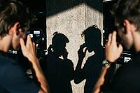 Shadow silhouettes of two young men reflected on a weathered concrete column reveal introspection, emotional vulnerability, psychological tension, urban alienation in subterranean darkness, symmetrical human outlines mirroring identical reflective gesture [IBR125446508]
