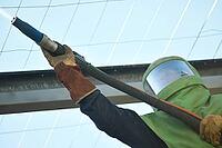 A man in protective clothing operates a sandblaster from a scissor lift to clean steelwork on a fire-damaged building, ready for repainting [IBR125448827]