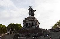Young people and tourists sit on the steps of the Deutsches Eck tourist attraction at the confluence of the Moselle and Rhine rivers, Koblenz, Germany [IBR125448863]