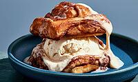 Sweet cinnamon roll piled high with vanilla ice cream. Creamy sauce drizzles down sides. Served on dark blue plate, AI generated [IBR125448878]