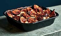 Roasted figs in a black baking dish on stone surface. Warm, caramelized fruit glistens under soft light. Dark background contrasts with rich, AI generated [IBR125448900]