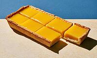 Sweet mango tart sliced into squares. One piece removed, revealing golden crust. Bright yellow filling contrasts with blue background, AI generated [IBR125448901]