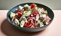 Fresh salad with tomatoes, cucumbers, onions, fennel, and yogurt dressing. Served in dark blue ceramic bowl. Vibrant colors, light background, AI generated [IBR125448902]