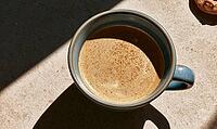 Top-down view of coffee in ceramic mug. Sunlight casts shadows on textured surface. Dusting of cocoa powder decorates the coffee, AI generated [IBR125448906]