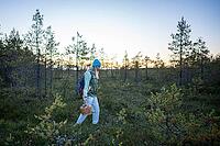 Woman walking out of autumn forest at twilight with basket full of mushrooms in hand. Female hiking in woods alone and enjoying nature, returning home after gathering seasonal forage in fall at dusk [IBR125462037]