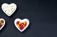 Heart shaped saucer filled with colorful sweets on a black background. Valentine's Day illustration. Top views with clear room [IBR125462057]