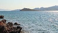 View of the coast at Bitez Bay shows clear blue Aegean sea water with sparkling sunlight reflections and rugged foreground rocks [IBR125462061]