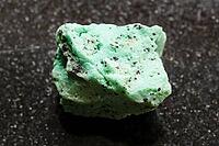 Specimen of mineral from geological collection - rough chrysocolla rock with black libethenite crystals close-up on black granite background from Alaverdi, Armenia [IBR125462094]
