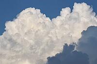 A majestic formation of towering, sunlit white cumulonimbus clouds against a deep blue sky, with dark grey shadows at the base, creating dramatic contrast and depth. [IBR125462099]