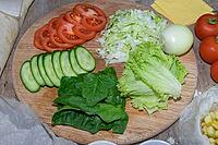 Preparation for the preparation of hamburgers. On a wooden board are lettuce leaves chopped: tomatoes, cucumbers, onions, sweets and sauces [IBR125462104]